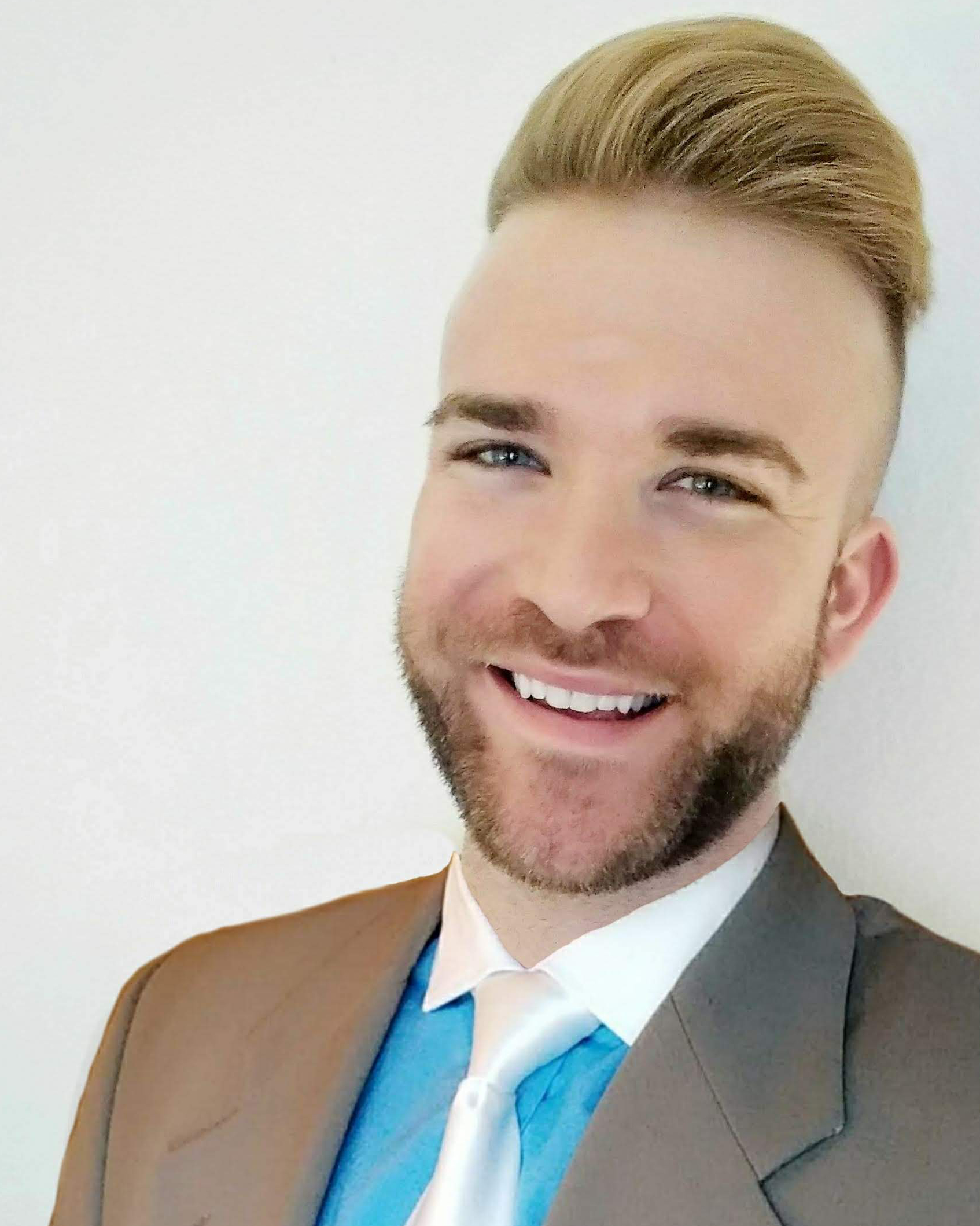 OCTA board member Michael Ritzel, wearing a brown blazer with white-collared teal button down shirt and white bow-tie. He is smiling with stubble and coifed hair