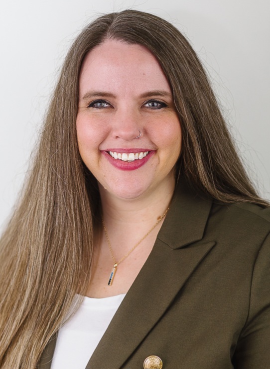 OCTA volunteer coordinator and secretary Rebekah Grieb, wearing a gold necklace, brown blazer and white shirt with brown hair, parted with the right side over the shoulder and left side behind.